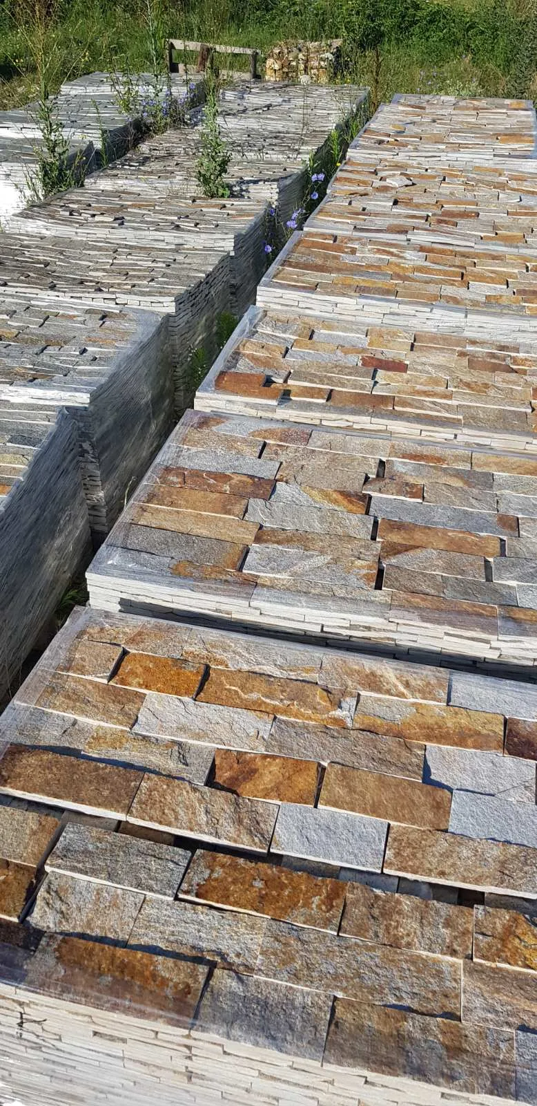 Palletized rustic gneiss wall strips stored outdoors at the production yard