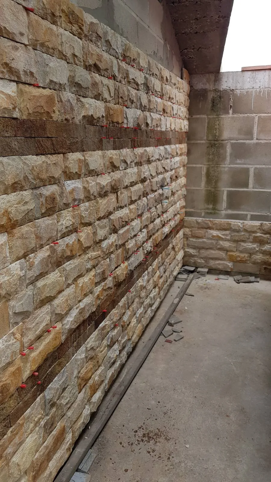 Courtyard wall being clad with cut gneiss stone strips during installation