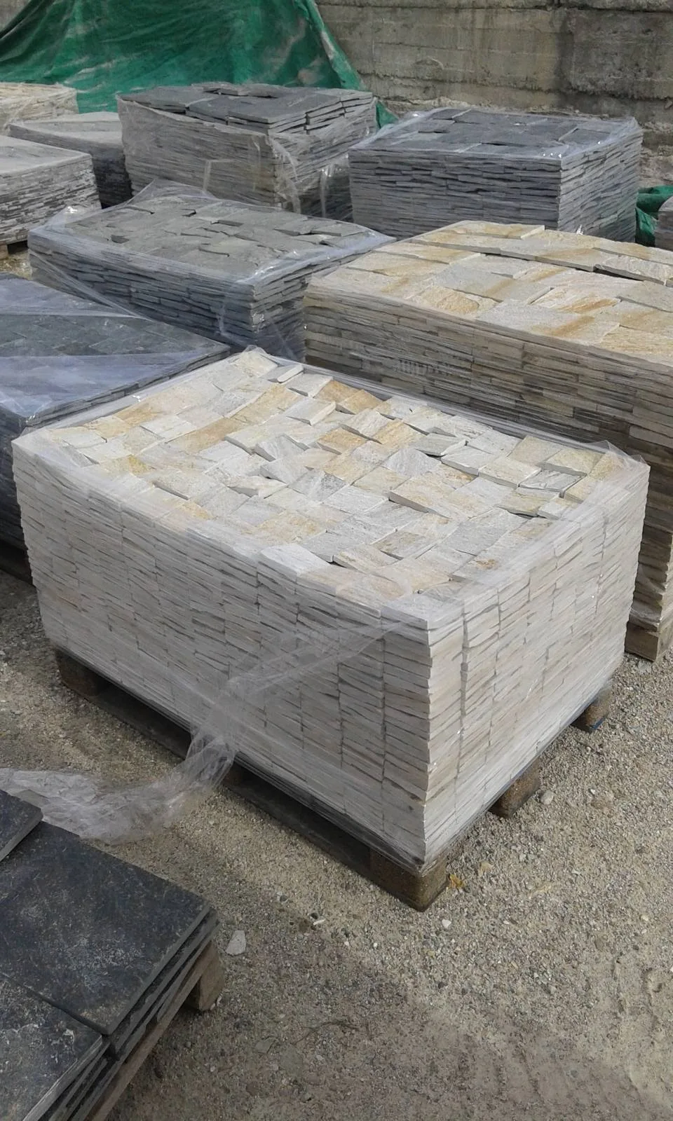 Wrapped pallets of cream and grey cut gneiss cladding stones in the storage yard