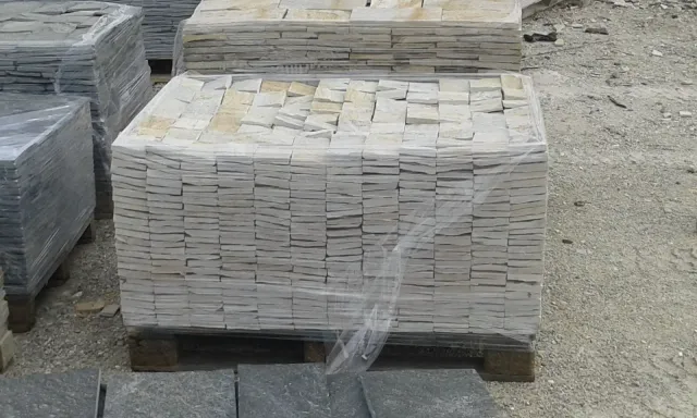Palletized white-grey gneiss cladding blocks wrapped in foil at the yard